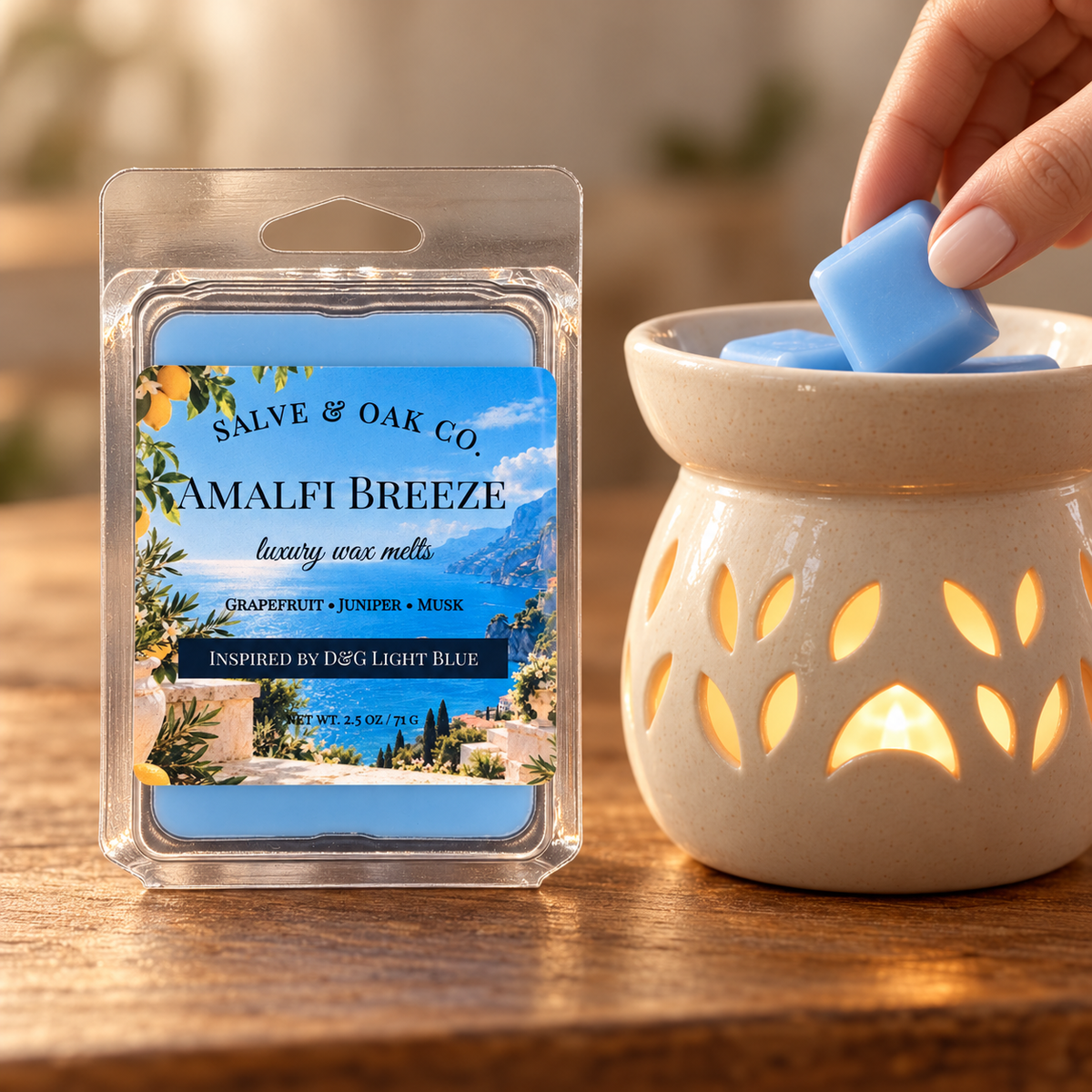 Hand placing a blue Amalfi Breeze wax cube into a glowing ceramic warmer beside its package.