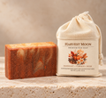 Harvest Moon grass-fed tallow and goat milk bar soap beside its muslin packaging on a warm neutral background