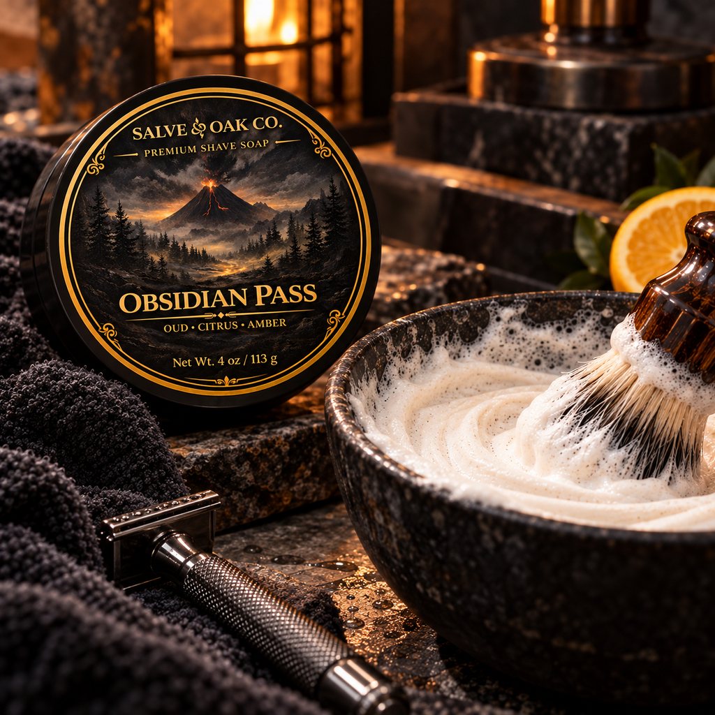 Obsidian Pass shave soap beside a lathered shave bowl, shaving brush, razor, and dark volcanic grooming setup
