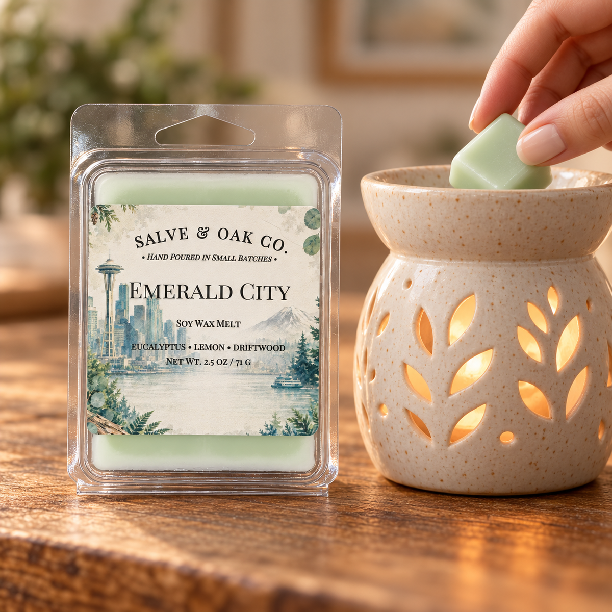 Hand placing a pale green Emerald City wax cube into a glowing ceramic warmer beside its package.