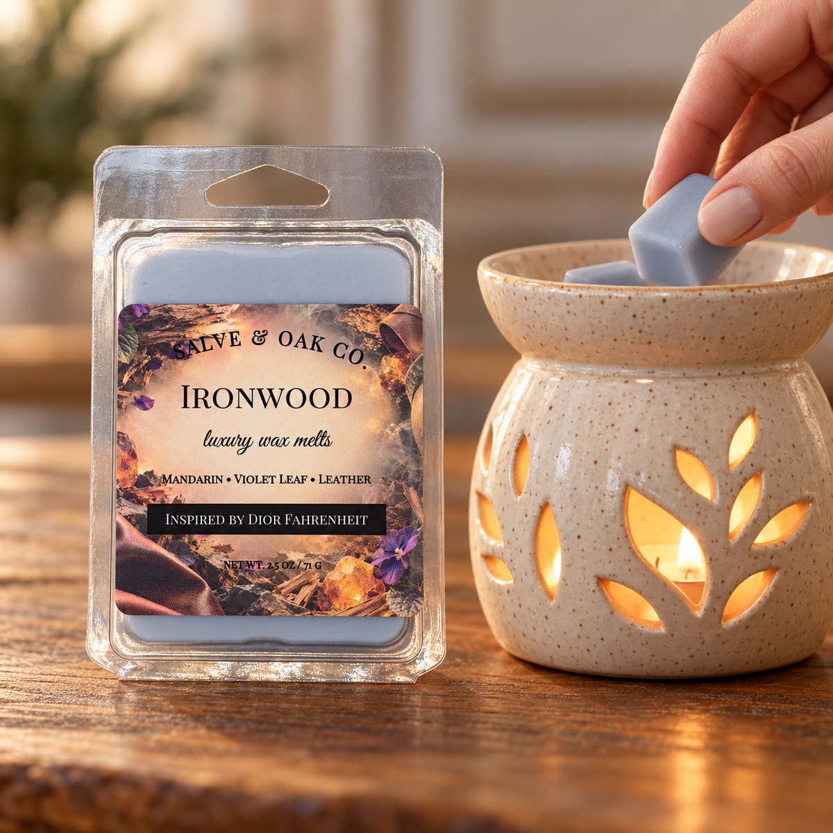 Hand placing a blue-gray Ironwood wax cube into a glowing ceramic warmer beside its package.