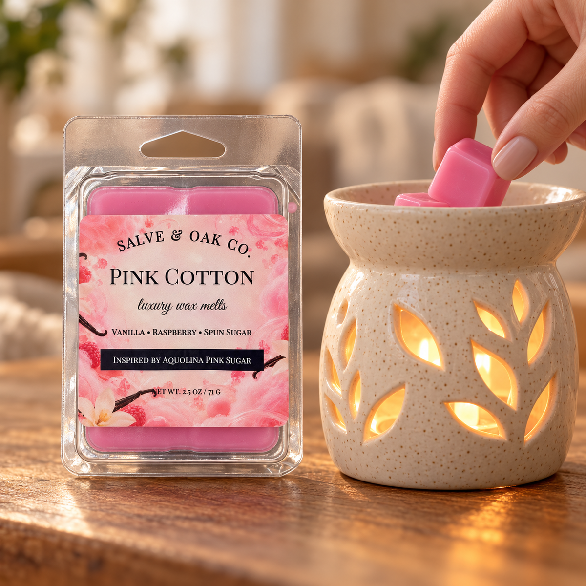 Hand placing a pink Pink Cotton wax cube into a glowing ceramic warmer beside its package.