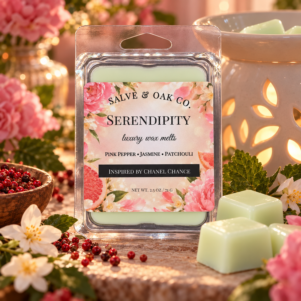Serendipity wax melts beside a glowing warmer, pink peppercorns, jasmine blossoms, and greenery in a blush floral setting.