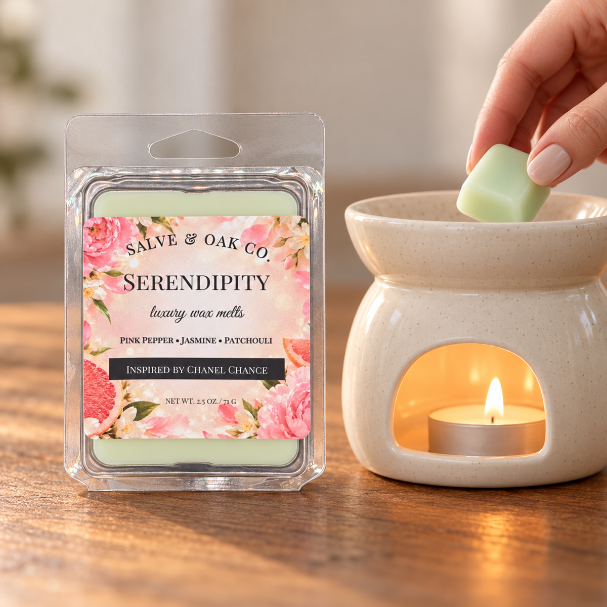 Hand placing a pale green Serendipity wax cube into a glowing ceramic warmer beside its package.