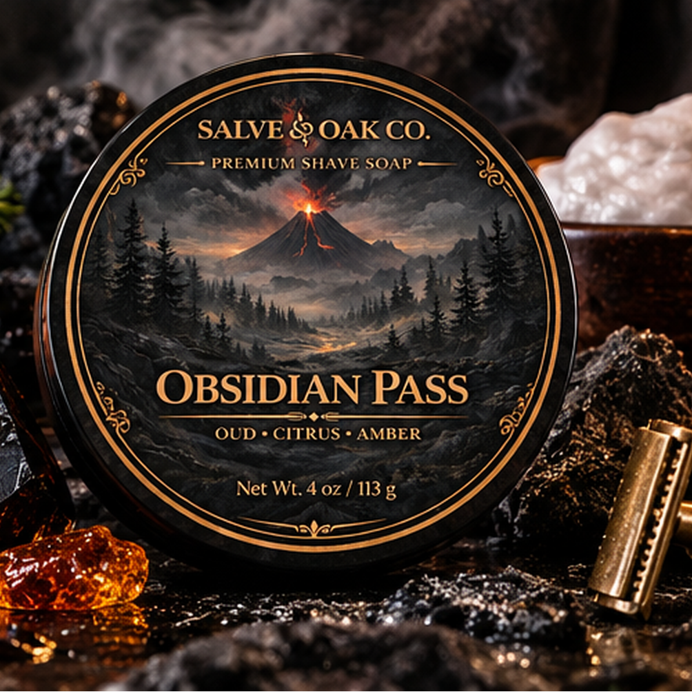 Obsidian Pass premium shave soap surrounded by black volcanic rock, citrus, amber tones, dark woods, and a dramatic mountain landscape